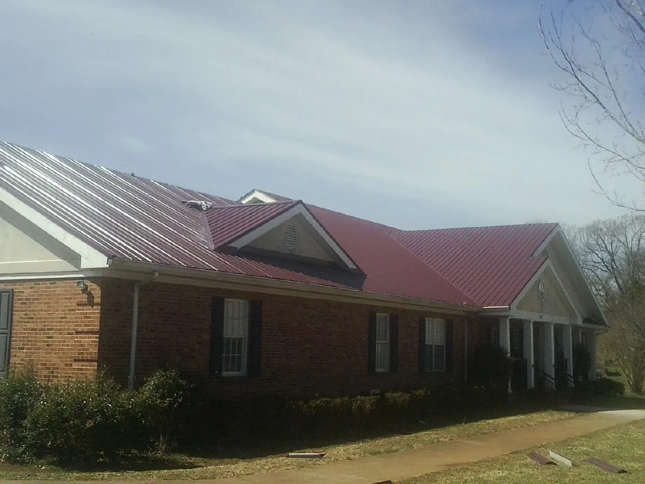 Red metal roof with gabled entries on a long brick building, from a Hail Damage Roof Repair job in Kokomo