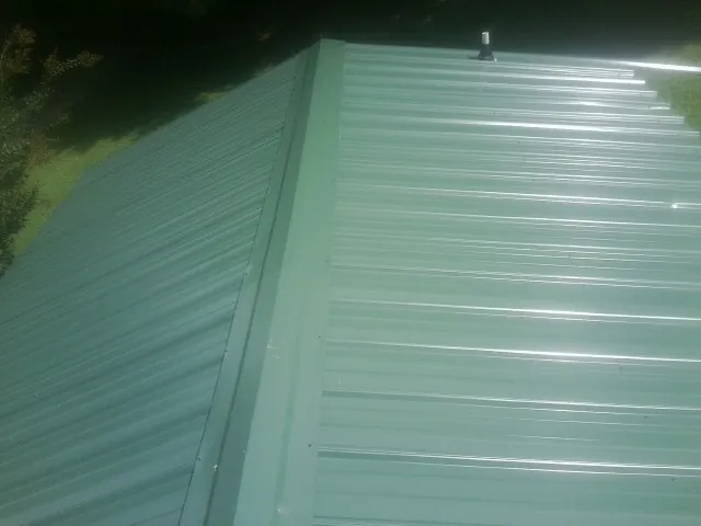 New green metal panels meeting at the ridge of a roof — Flat Roof Repair work by our crew in Kokomo