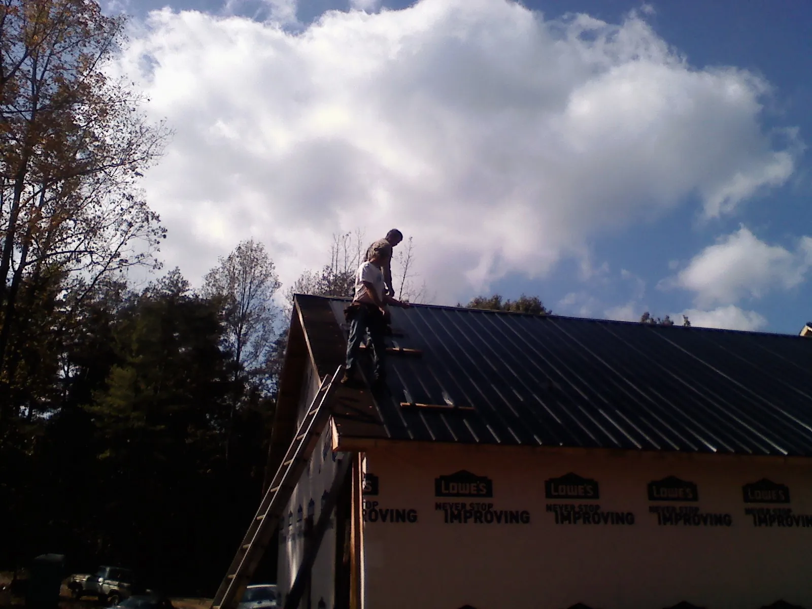 Roofer fastening dark metal panels high against a cloudy sky, from a Roof Inspection job in Kokomo