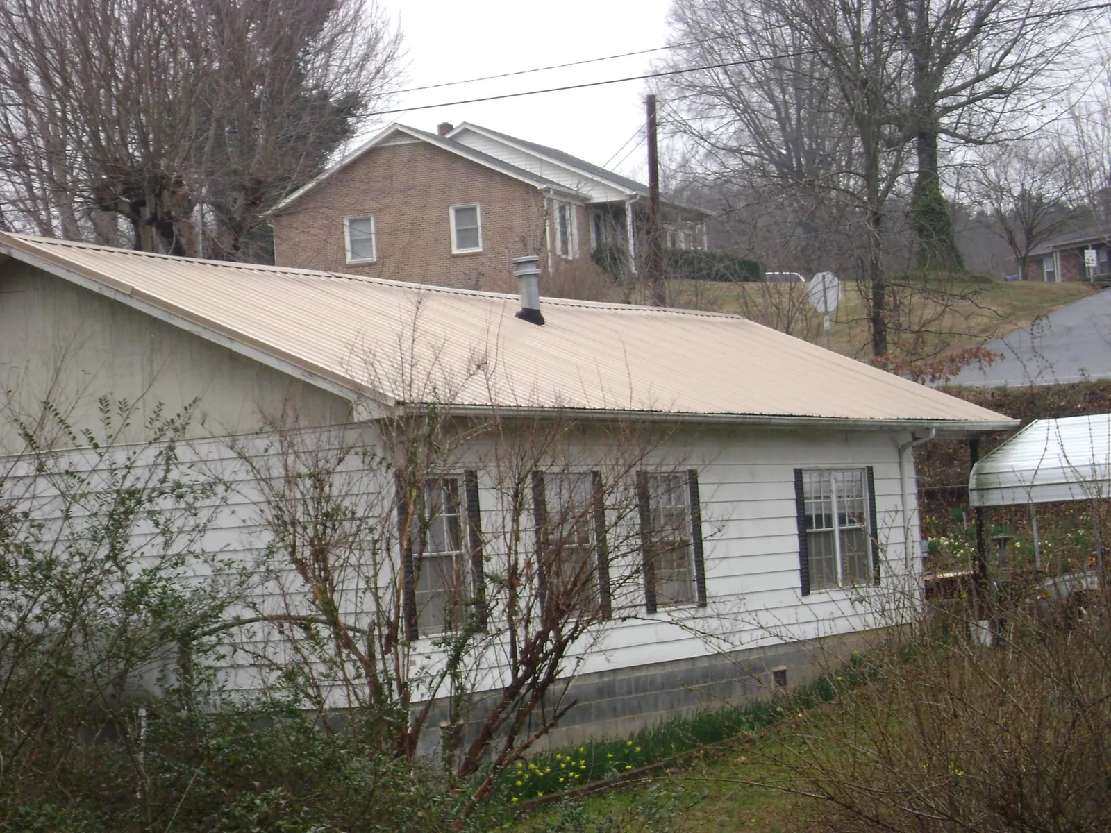 Tan metal roof on a white sided house set into a hillside — Commercial Roofing by Roofing Brothers in Kokomo