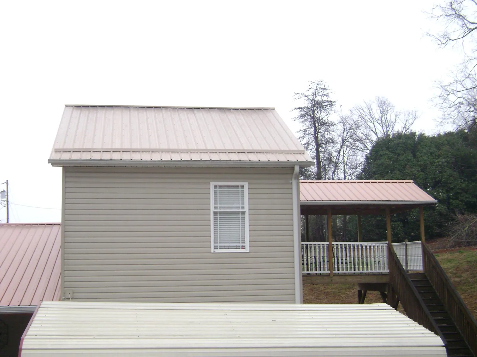 Tan metal roofs on a two story addition and attached porch, from a Roof Replacement job in Kokomo